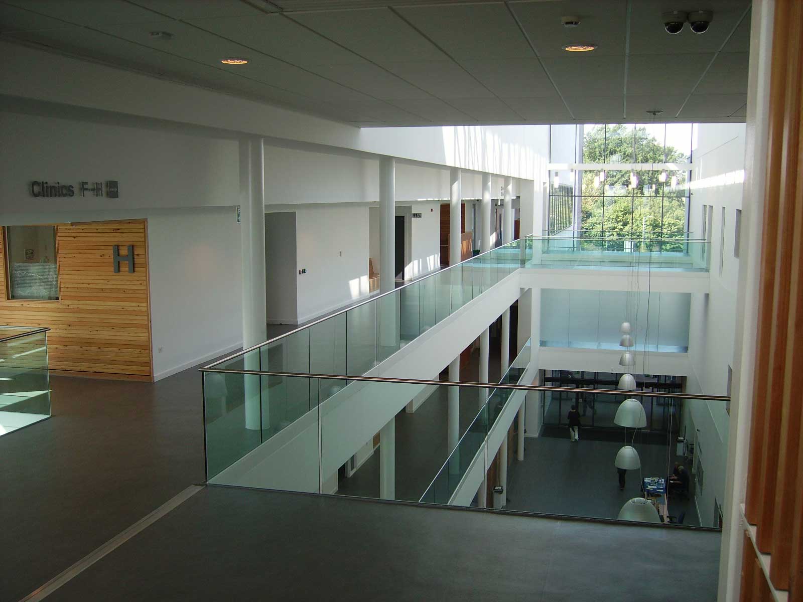 A view across the atrium of a hospital - you can see doors into individual offices over two floors and a large expanse of windows at the back looking out towards trees and greenery 