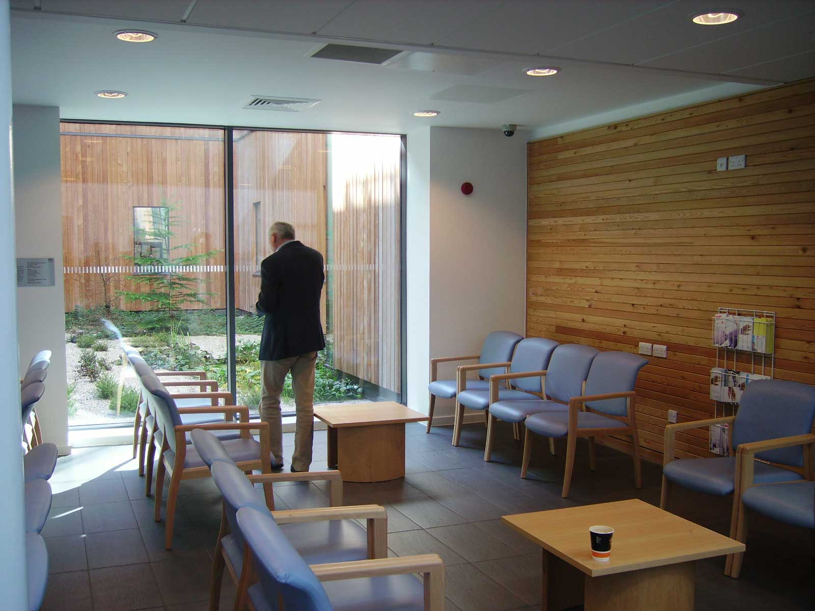 A waiting area with a large window looking out into a garden space, a man stands in front of the window