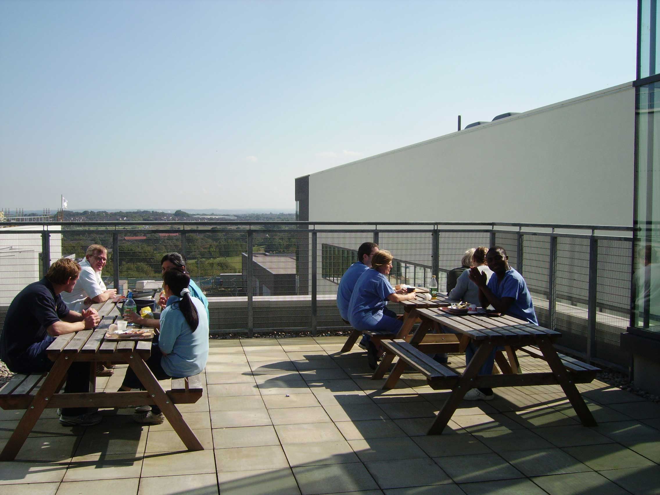 An outdoor terrace with picnic tables with groups of hospital staff sitting in the sunshine