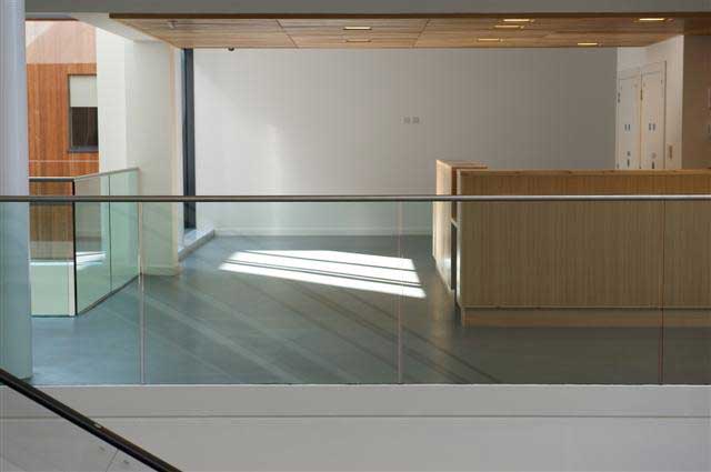 A photograph of an empty reception area with a wood-clad reception desk behind a glass balustrade 