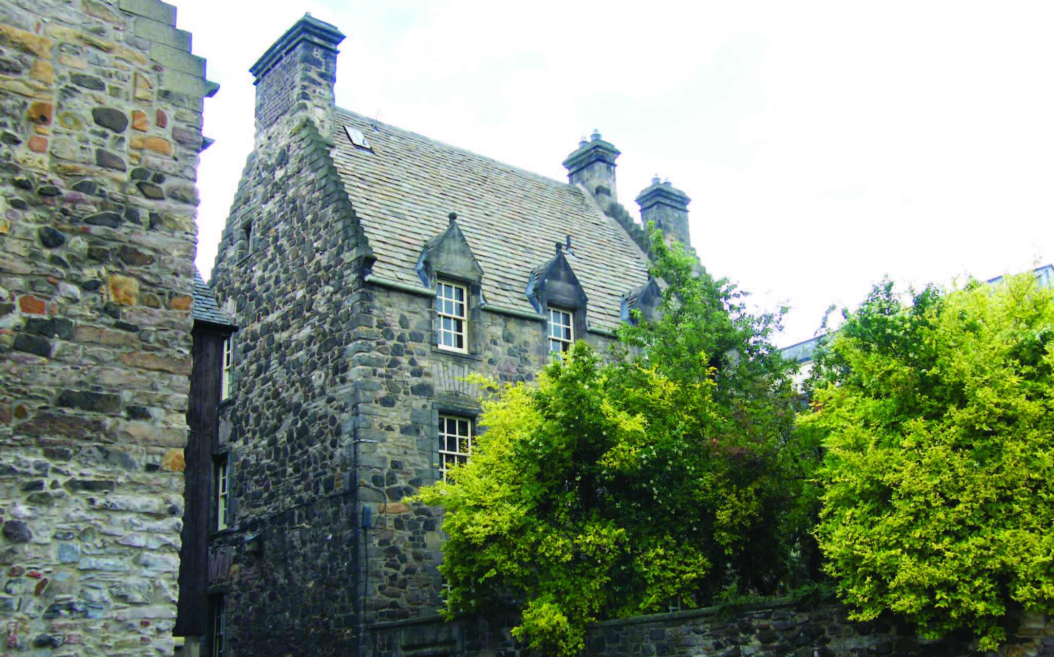 A heritage stone building and a courtyard with bright green trees. The roof of the building is made of slate.