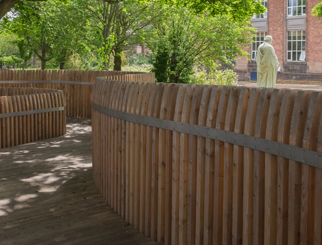 A wooden pathway in Arcadia Nursery Gardens with vertical timber walls alongside it. 