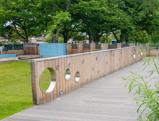 A timber wall with portholes made of metal separates a green area in Arcadia Nursery Gardens.