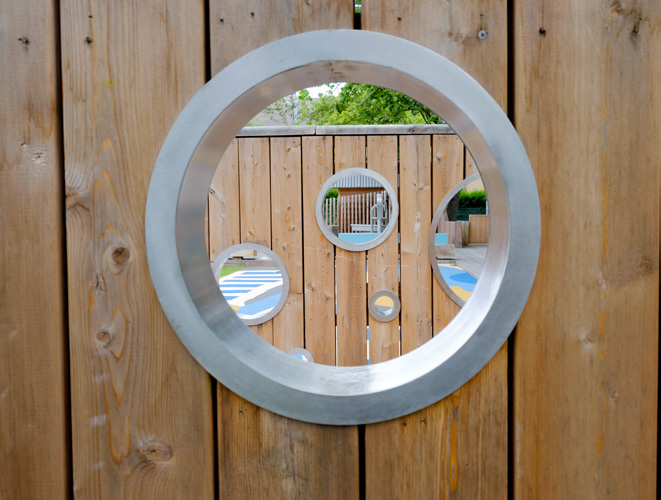 A close-up of one of the portholes that line the timber walls in Arcadia Nursery Gardens. The play area is visible through the hole.