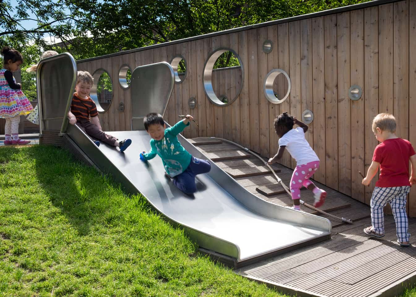 Kids from Arcadia Nursery playing on a slide with grass beside it in the garden.