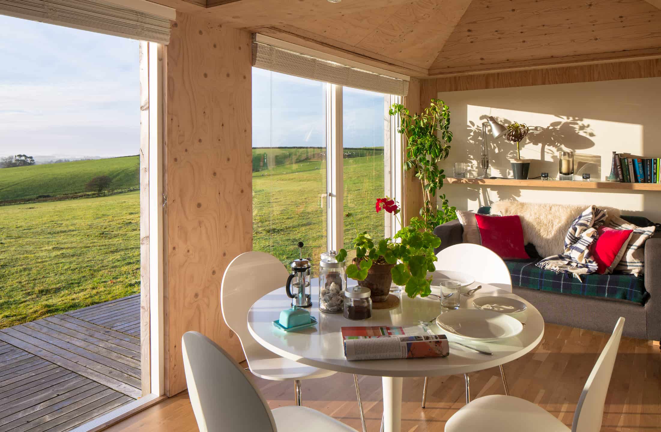 A dining table with wide windows overlooking a rural landscape.