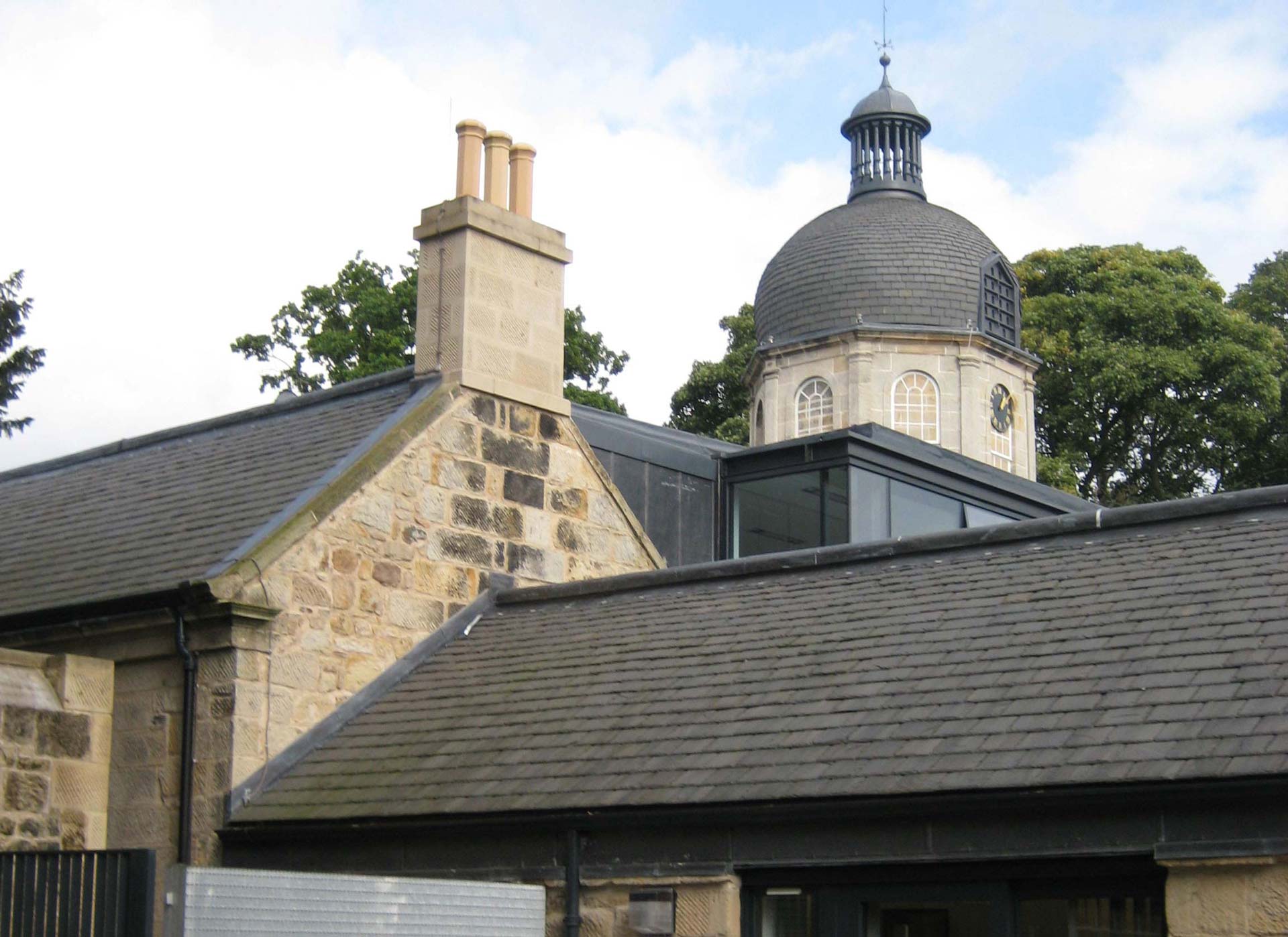 A close up image of the roof top of a converted stables building made from stone, with the view of a clock tower in the background