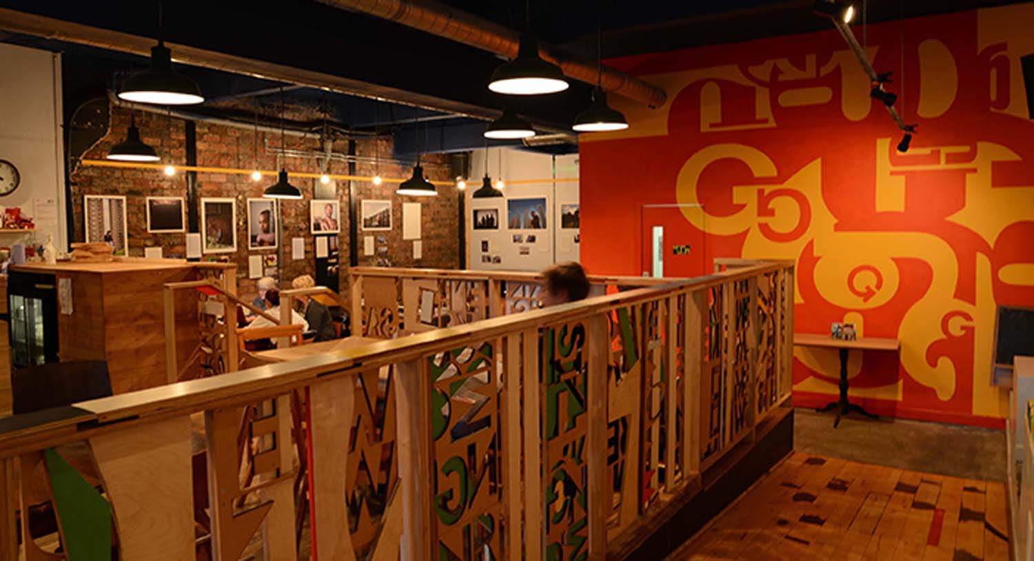 A pony wall separates a section of the Glad Cafe seating area. The pony wall is made of timber and has cut out letter stencils.