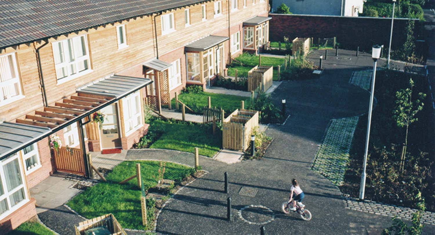 An aerial view of a child cycling on a car-free street in front of a row of terraced houses.