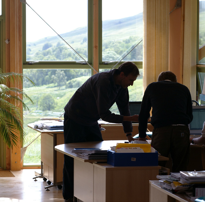 Two people looking down on a stack of papers on a work table in an office. The office overlooks a rural setting seen through its floor to ceiling windows. 