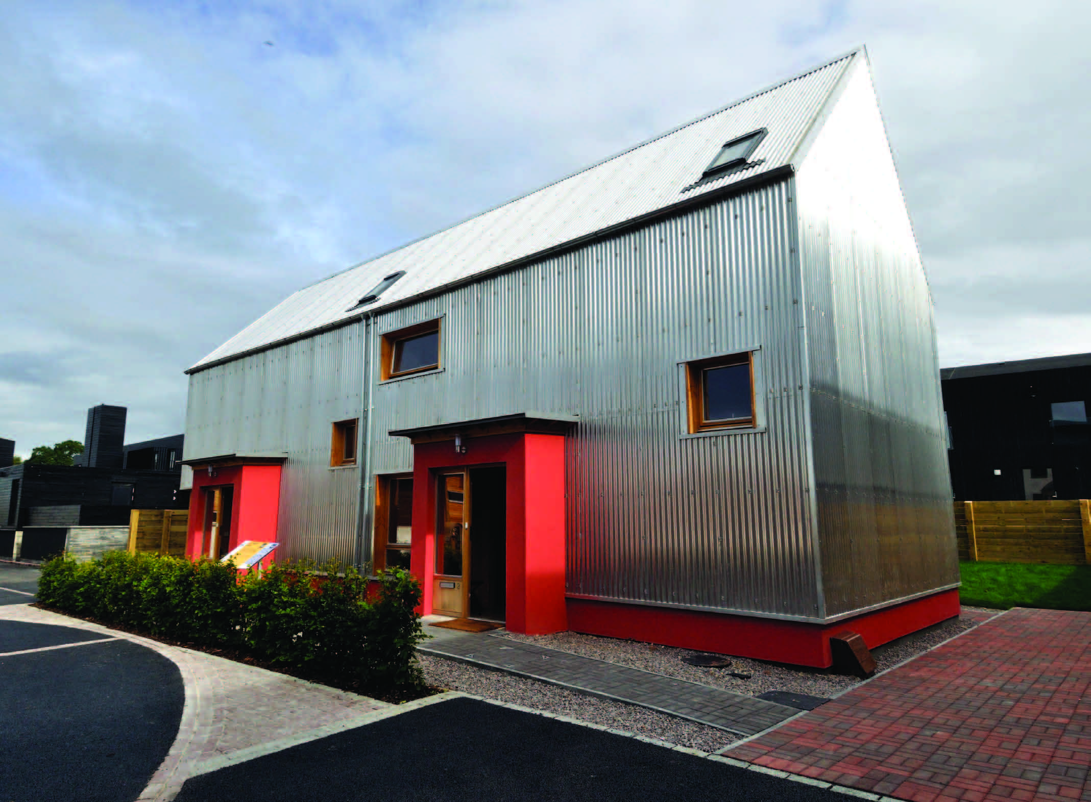 Two semi detached building covered in aluminium sheet and a red painted feature on the bottom half of the ground floor.