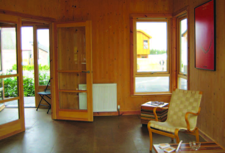 The ground floor living area in the Timber House with double doors leading to the house's entrance. The walls have a unpainted natural wood finish.