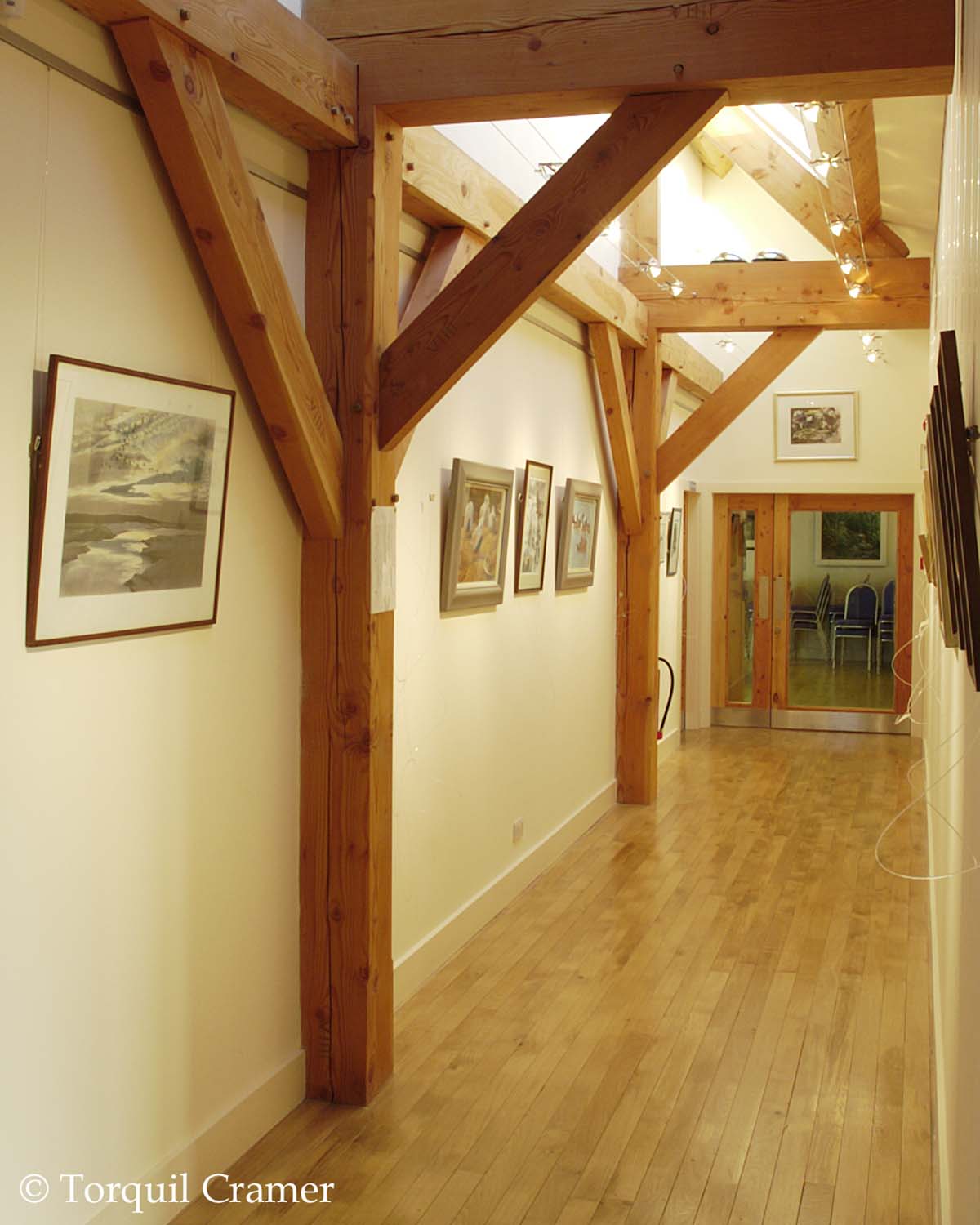 A hallway gallery with exposed wooden wall and roof beams. The flooring has a wood finish and white painted walls.