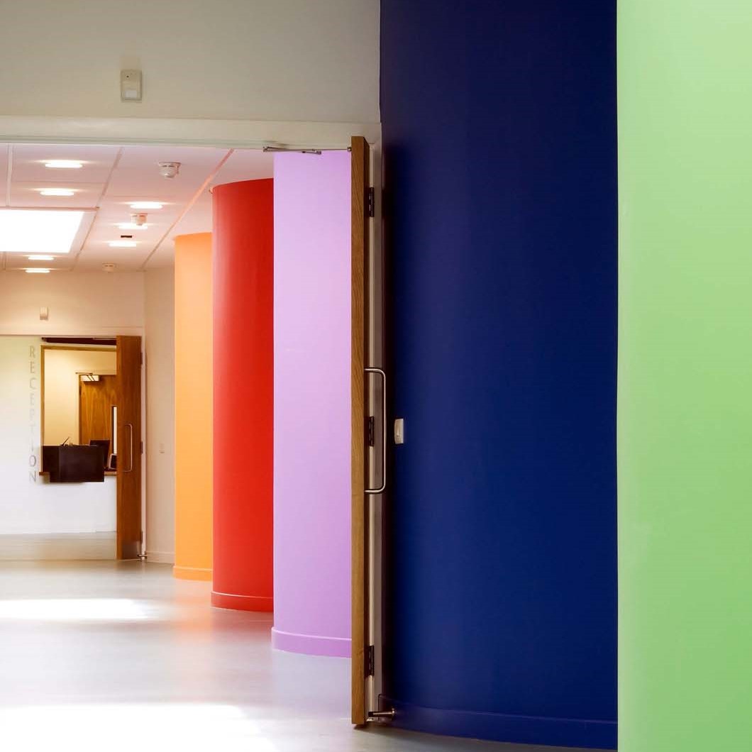 A corridor with a series of brightly coloured curved walls - the walls are green, purple, pink and red