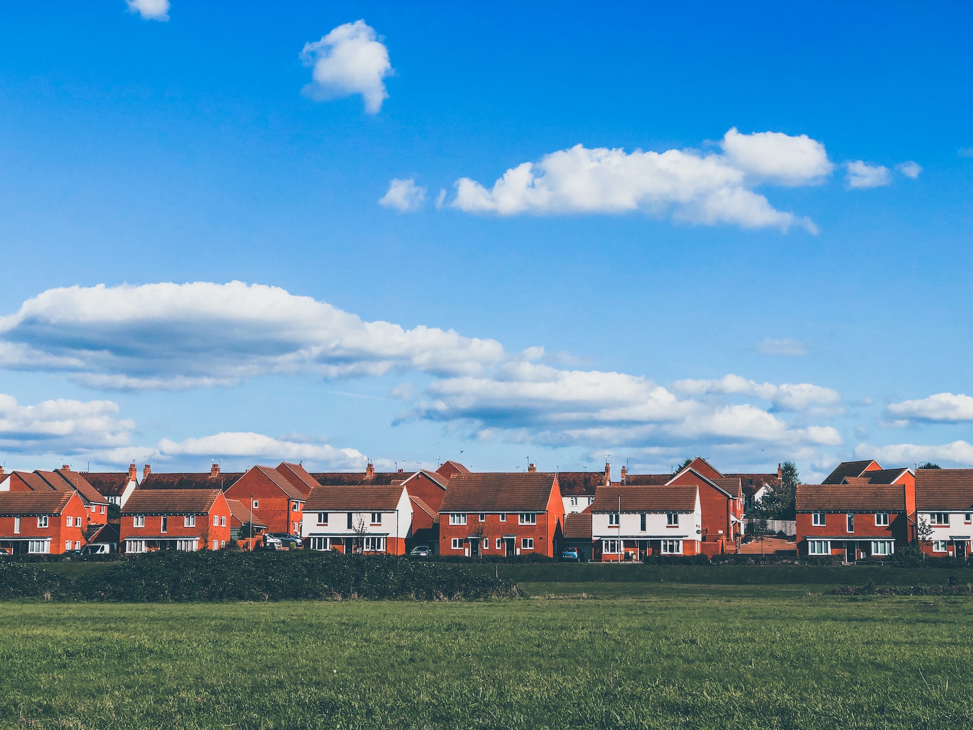 A photograph of a housing estate viewed from across a green field with a blue sky above 