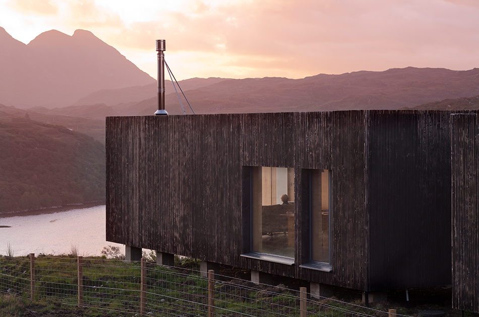 A closer look at the exterior larch cladding from An Cala House. Mountains and a loch can be seen in the background.