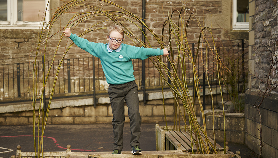 A pupil walks above an outdoor seating area that has planters and a growing willow tree at St Mary's Dunblane.