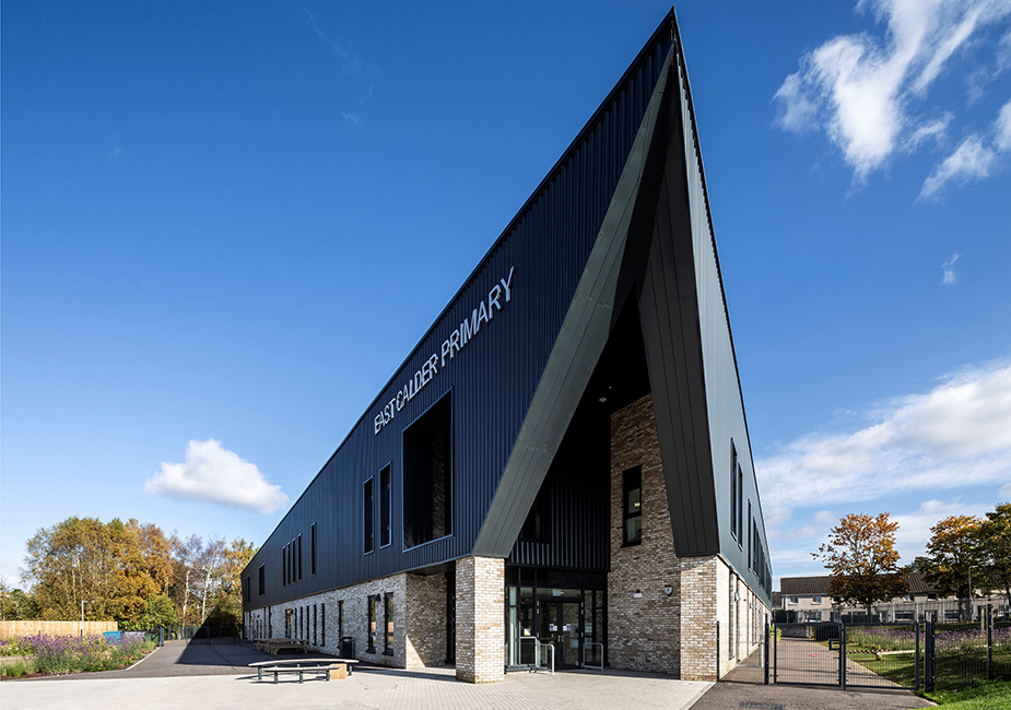 Modern East Calder Primary school features a striking angular design, with a blend of black metal and brick facade against a blue sky.