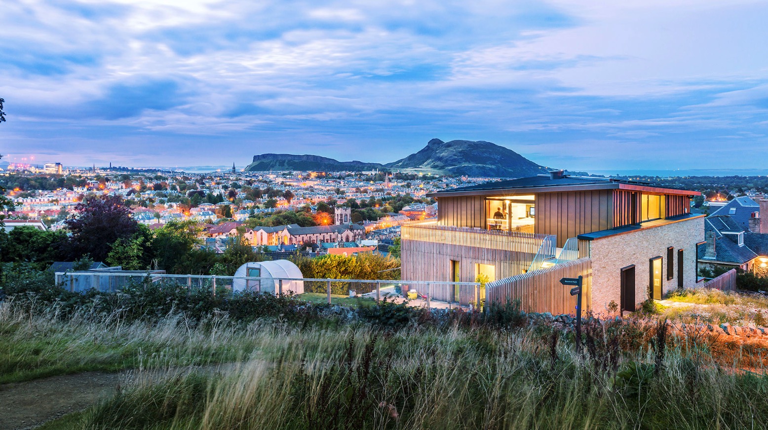 A modern house building with larch cladding with Arthur Seat and the Crags in the distance.