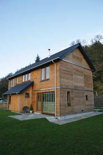 A detached two-storey house in Kilmun with green grass at the entrance. The house has a grey roof and horizontal wood cladding across both floors.