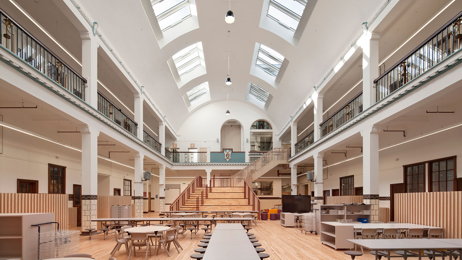 The interior of a two-storey atrium in a school. The ground floor of the atrium is a cafeteria and the first floor leads to the classrooms.