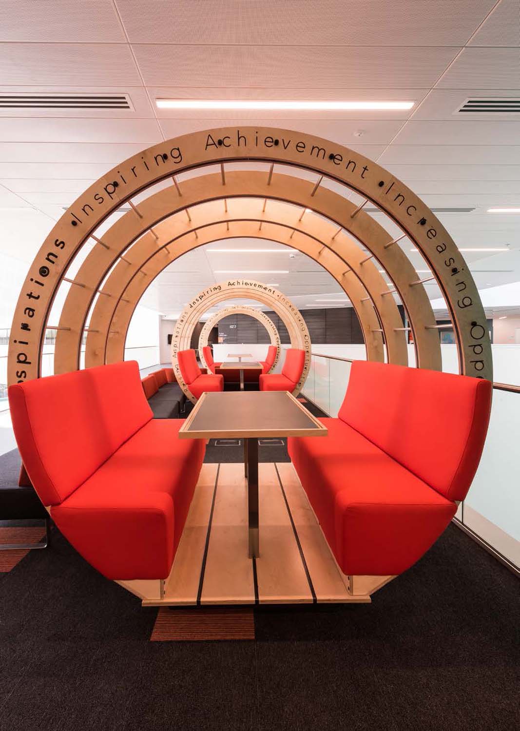 A circular wooden structure with orange upholstered seating and a table 
