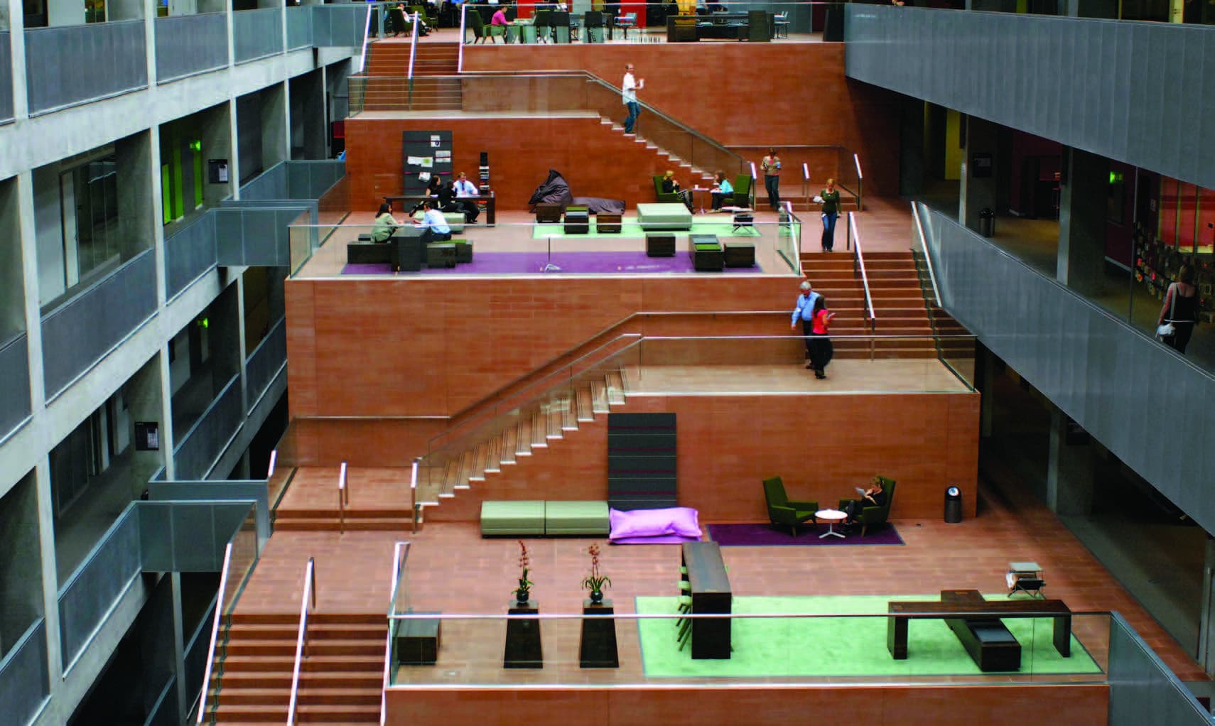 A stone street stairway in a centre of a modern building. Sections of the stairway have seating areas and social spaces.