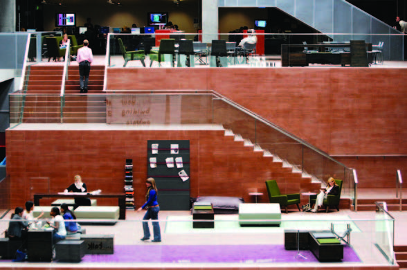 A large atrium space with red coloured stairs leading up to the next floor, with seating area on the ground floor