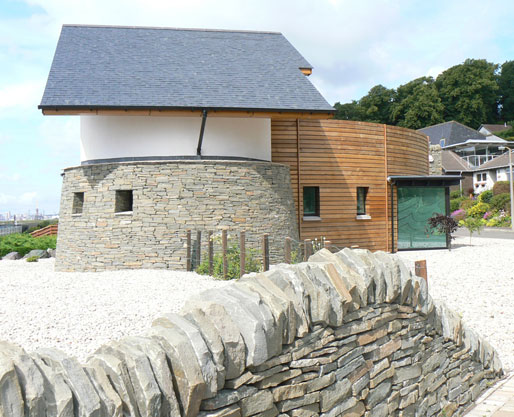 Exterior view of a home with a rounded stone building and a timber entrance area on the right hand side