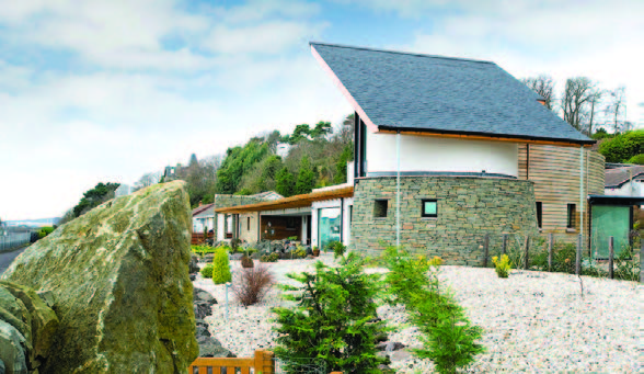 An external view of a house which features stone and timber, sitting at the top of a white driveway 