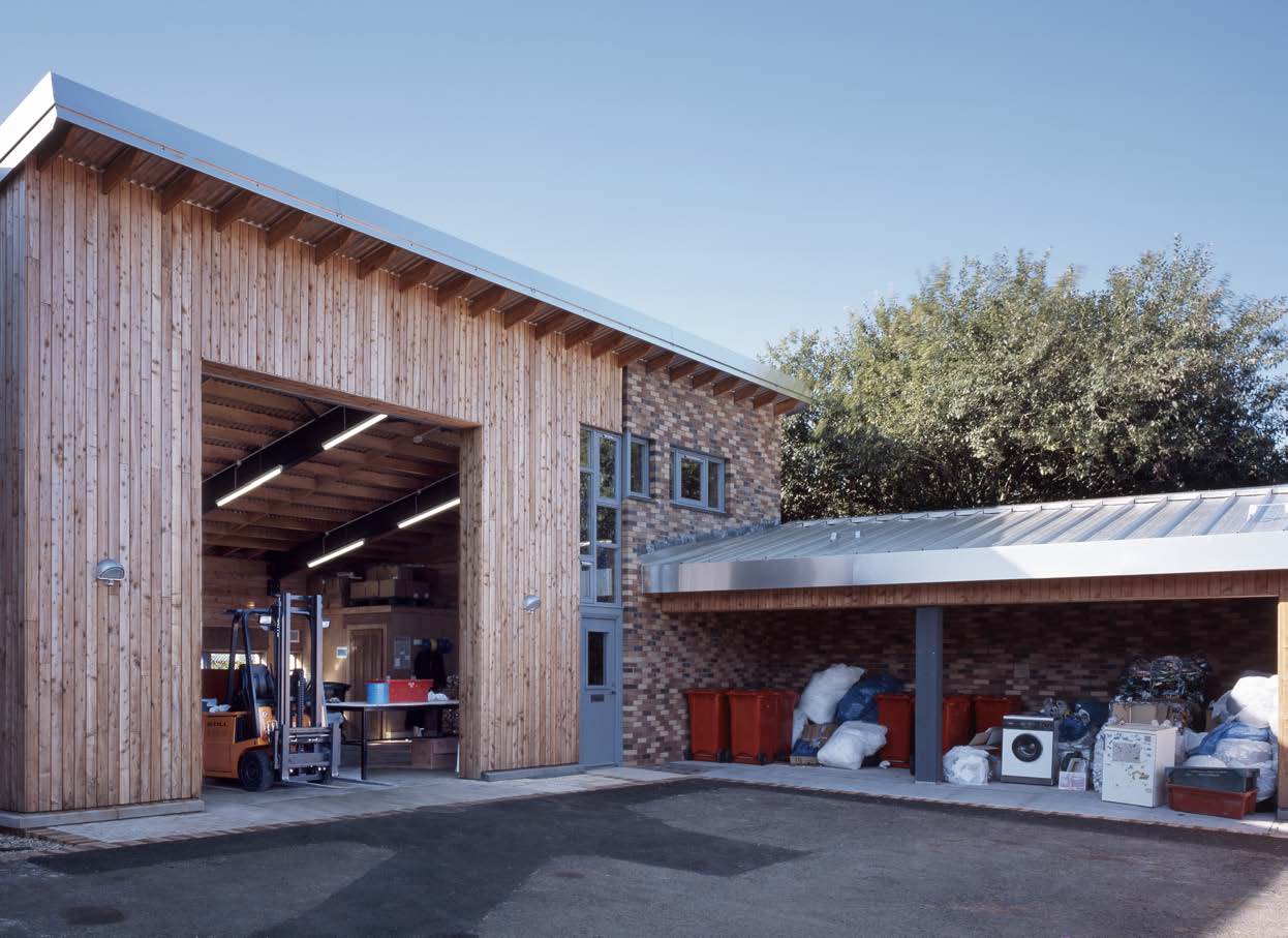 An exterior photograph of a large timber and brick built shed with a double height door with a covered storage area on the right forming a courtyard