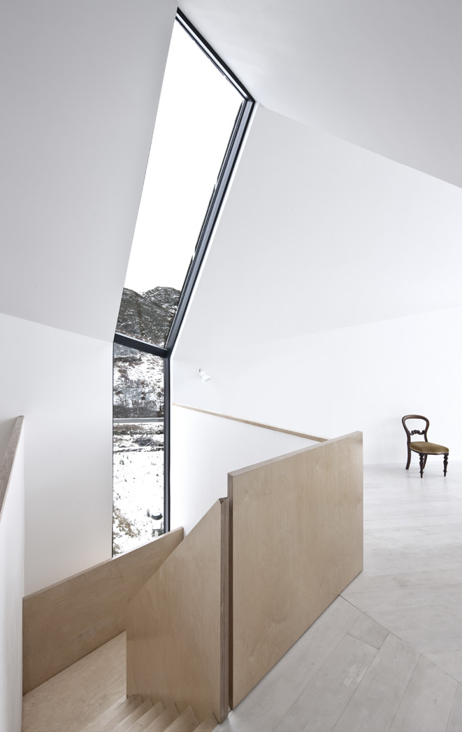 The stairwell at Camusdarach Sands with windows reaching the entire length of the wall and roof and natural wood panel bannisters.