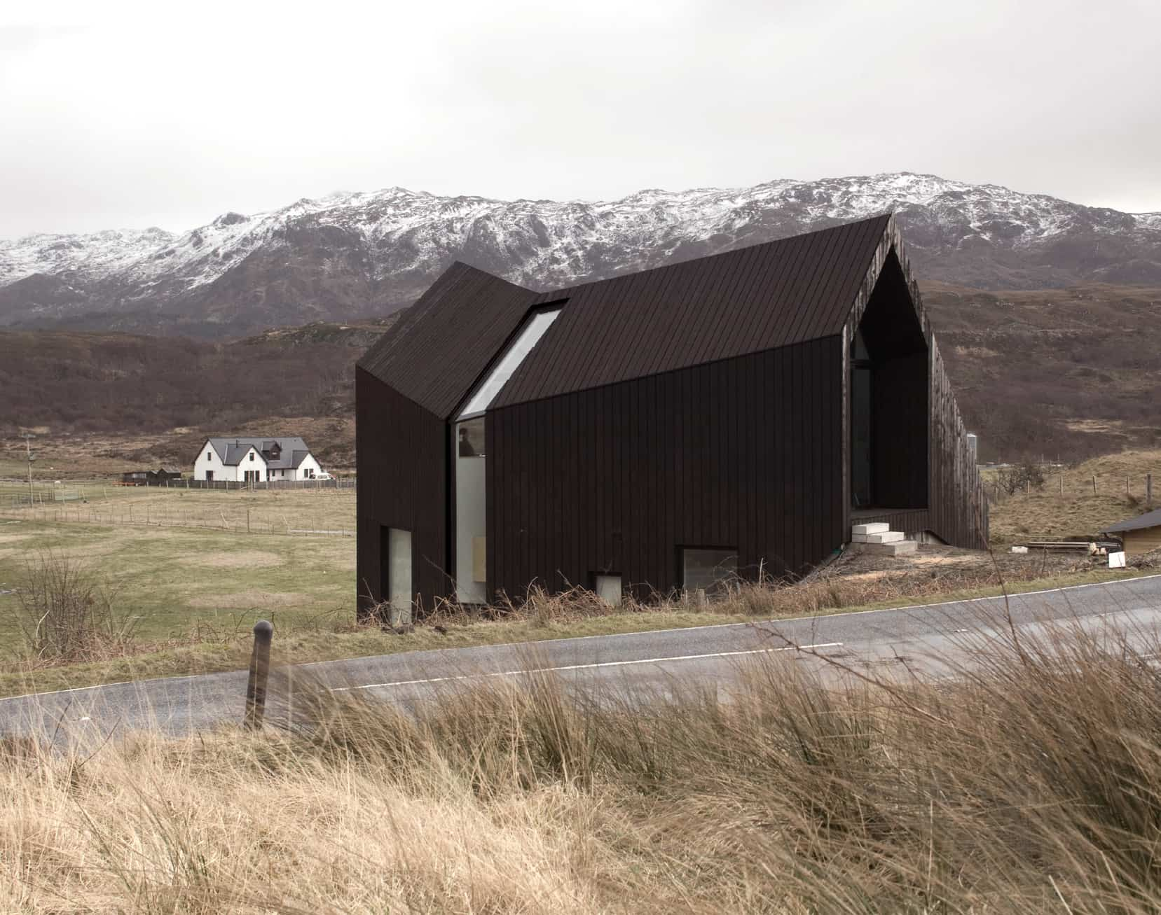 A view of the House at Camusdarach Sands from the street showcasing white-capped mountains in the background.