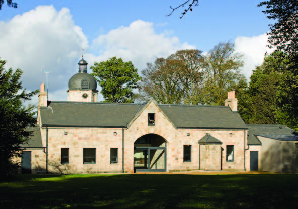 A low rise yellow sandstone building with a large arched entrance