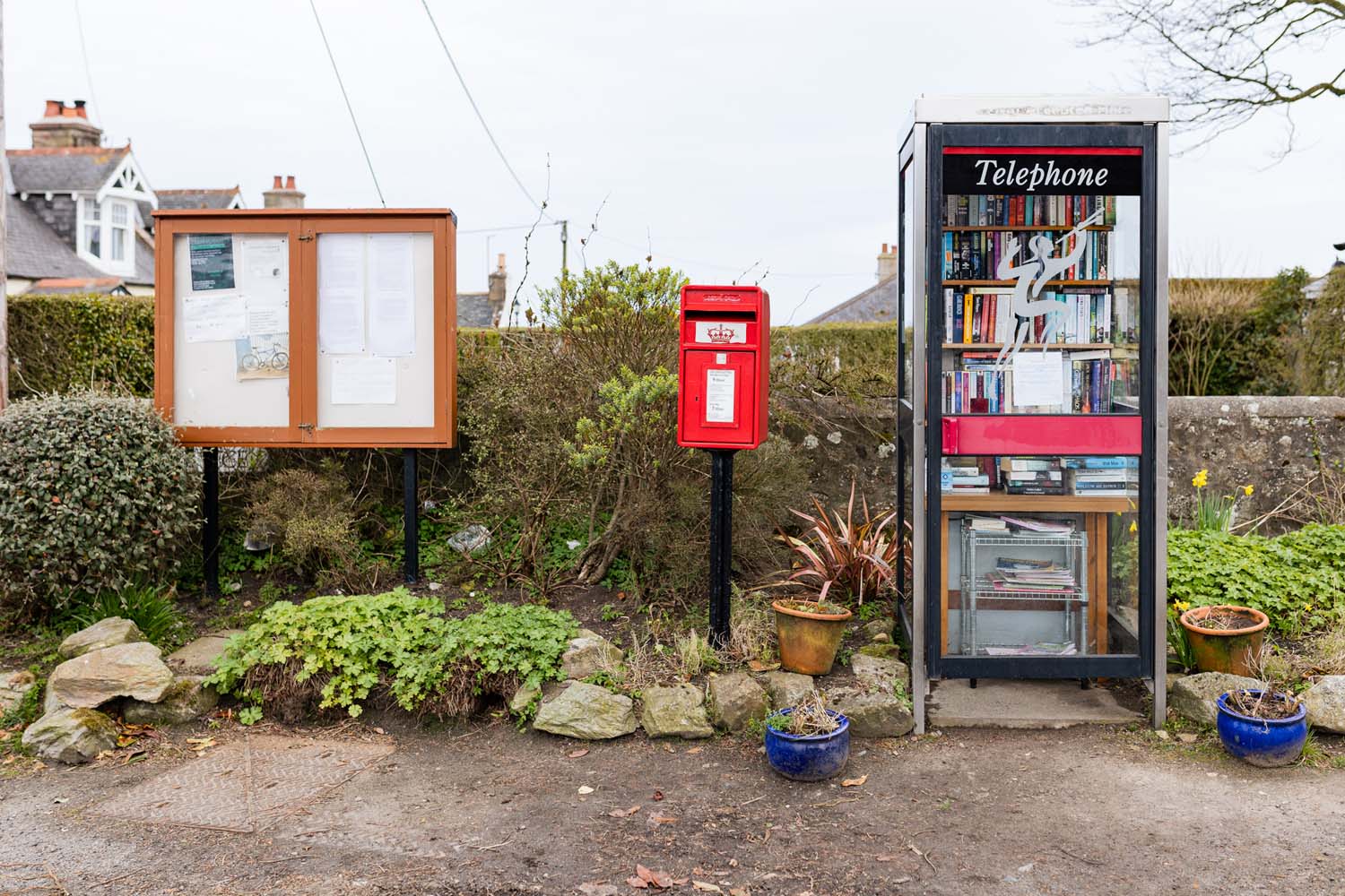 A community noticeboard, a red postbox and a phone booth side by side. 