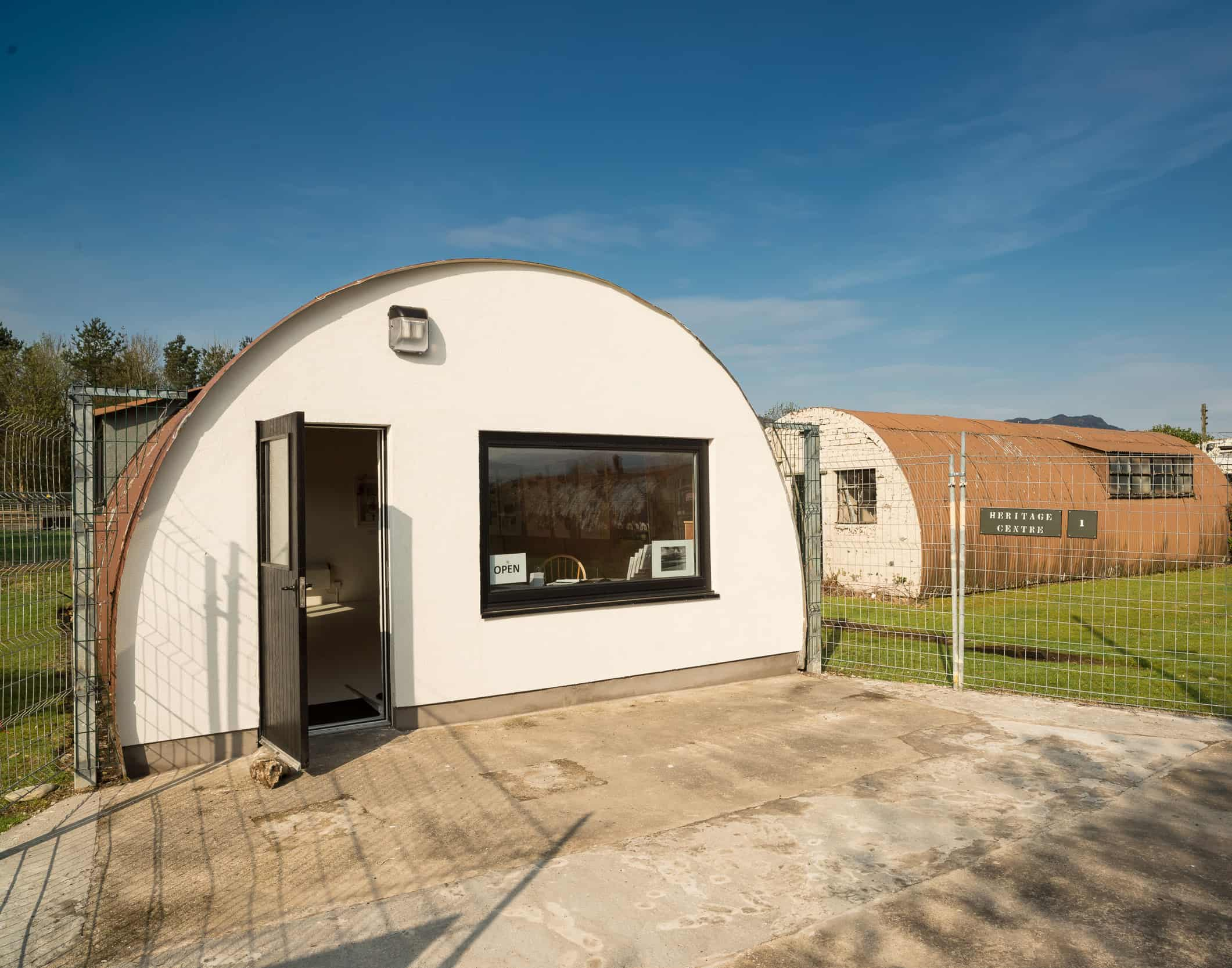 The entrance to a hut that is semi circle in shape. The entrance wall is painted in white and the door and window frame is black in colour..