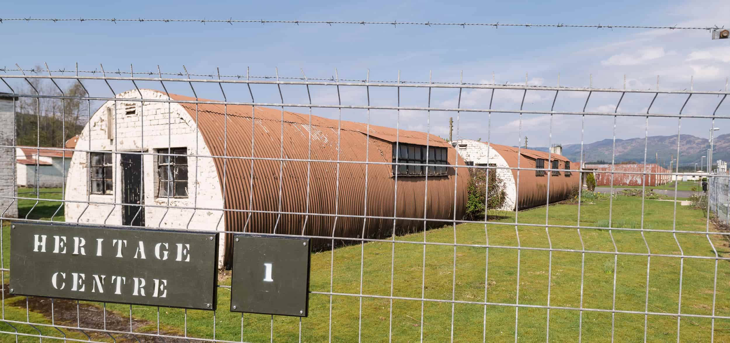 Two semi circle shaped buildings. The entire building is covered corrugated metal sheet in pale red colour with white brick wall as the entrance.