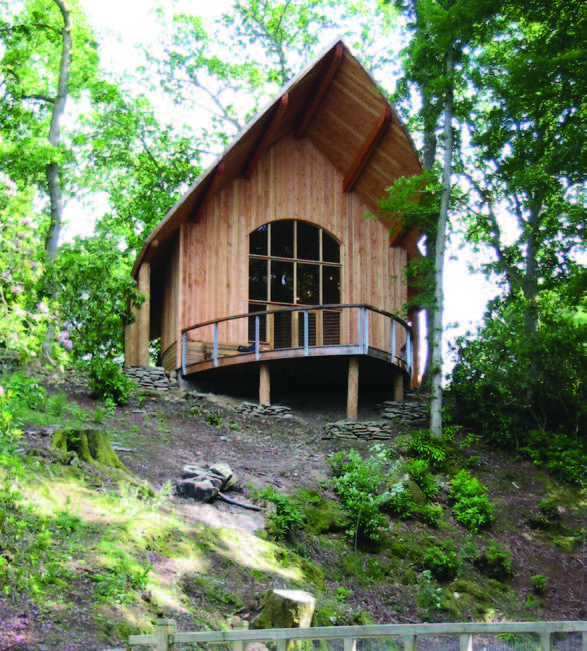 A wooden building set into a hill surrounded by trees with a bow shaped viewing balcony 