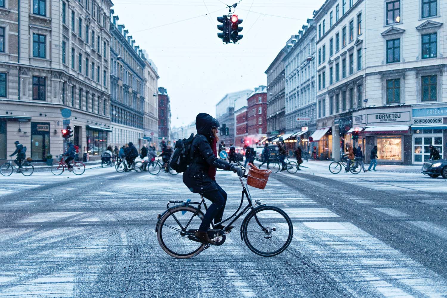 A young woman cycles across a junction in Copenhagen on a snowy day. 