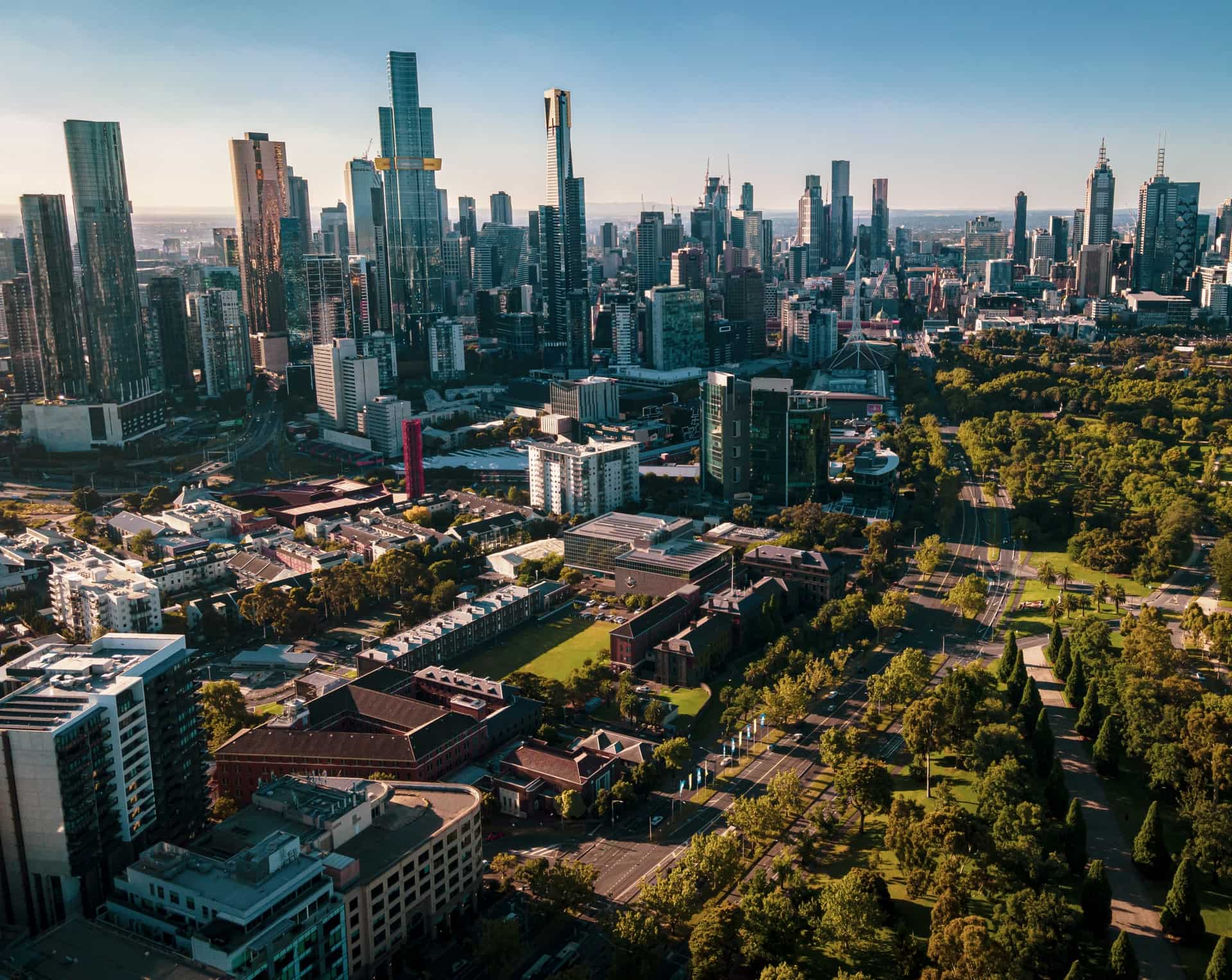 An aerial shot of Melbourne on a sunny day showing skyscrapers, trees, and roads.