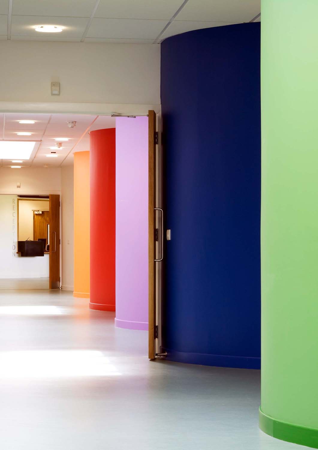 A corridor with a series of brightly coloured curved walls - the walls are green, purple, pink and red