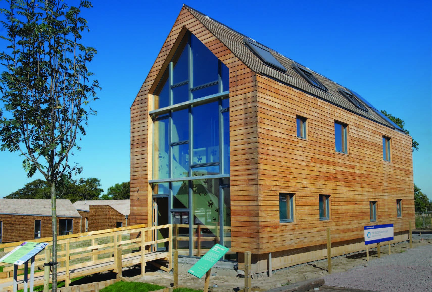 A two-storey house covered in horizontal timber cladding façade with flower details and a large floor to ceiling window at the entrance.