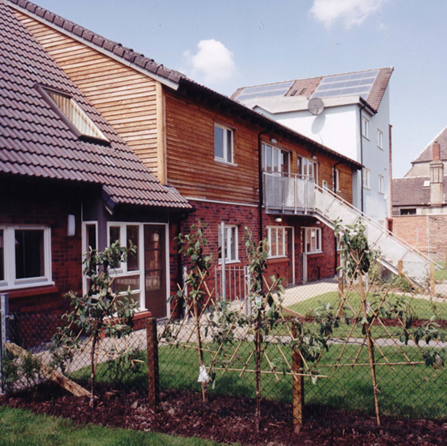 Timber and brick-cladded terraced houses and a flat block. Solar panels are located on the flat block's slanted south-facing roof.