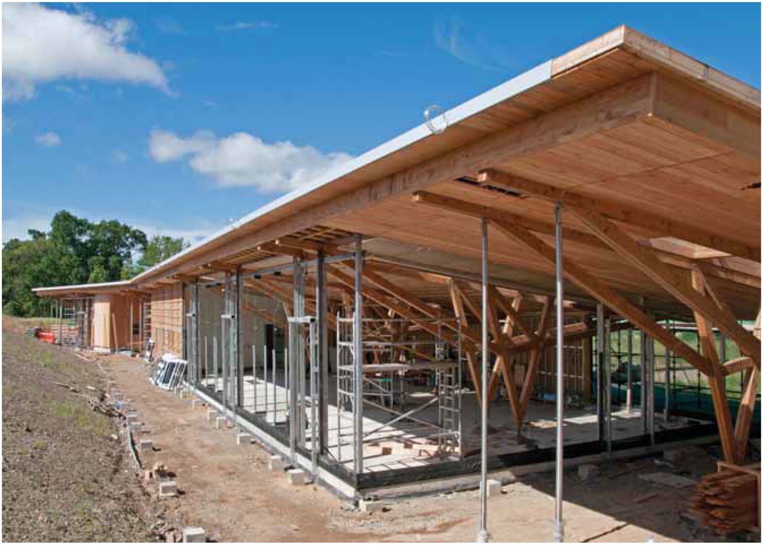 Construction site of Glentress peel. A half built long building structure made of timber placed on a slight slope with trees in background.