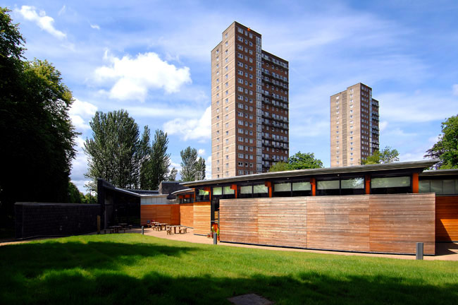 A single storey school building with a curved timber wall and red details. There are high rise buildings visible in the background.