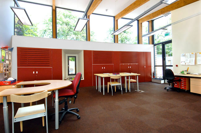 A close up of a school's social area, with large windows and a table set against some bright red cupboards.