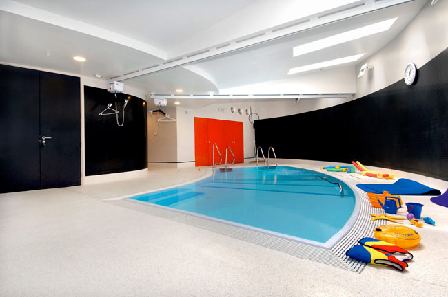 An interior small curved pool. There are two dark painted walls on either side and a set of brightly coloured red lockers.