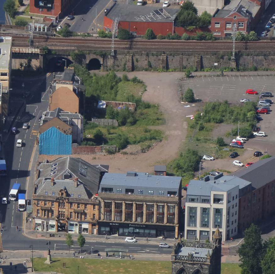 An aerial shot of the Paisley town centre showing a parking lot and an empty space behind existing buildings.