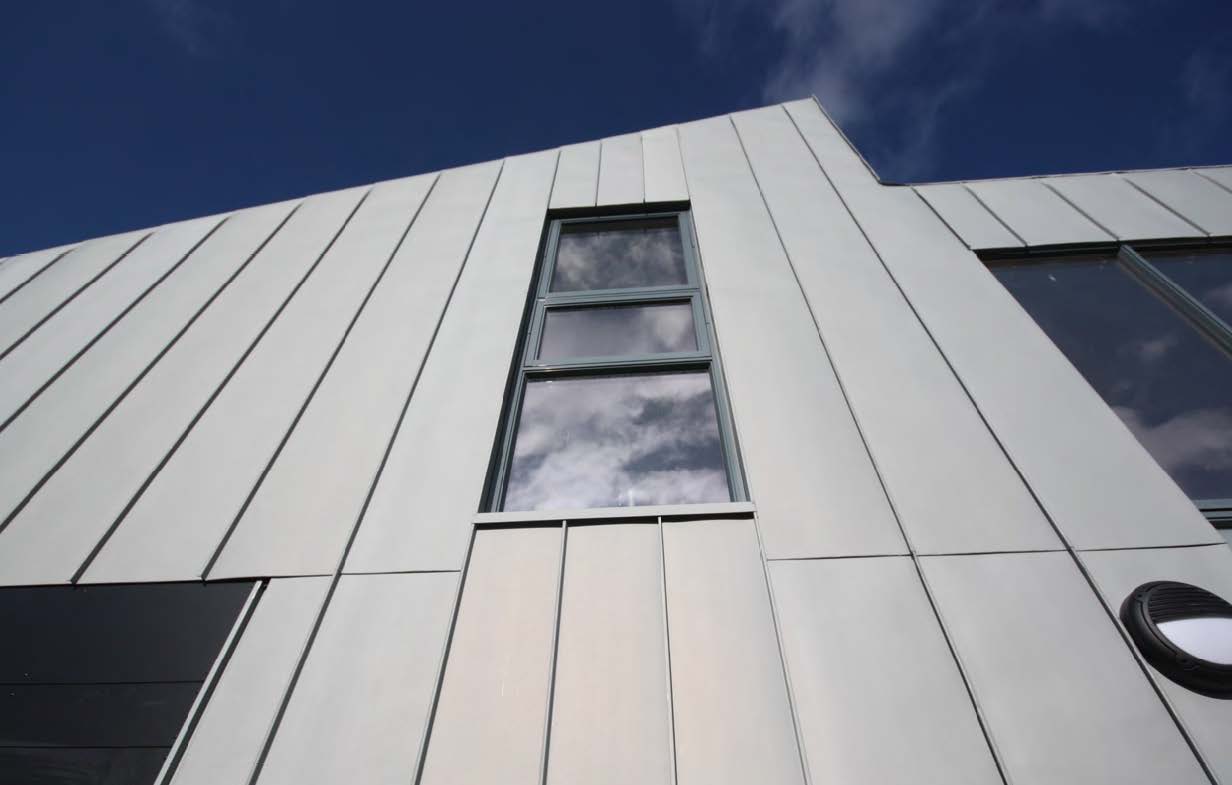 A close up photograph of a wall that is clad in zinc and with a various shaped windows