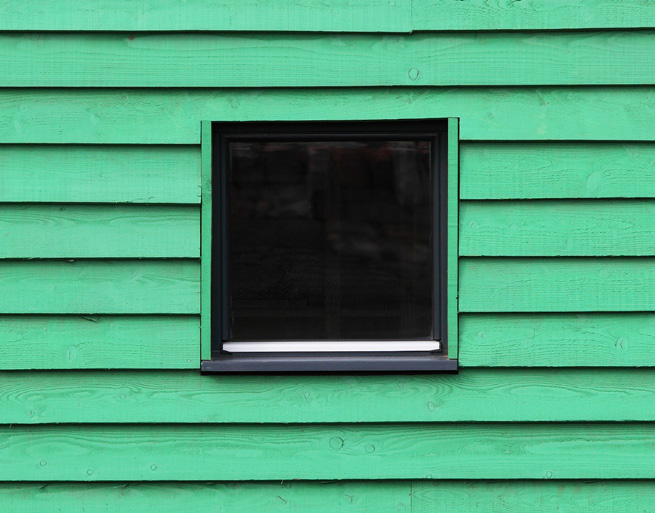 A square window on a bright green painted external wall. The wall uses horizontal slats of wood.